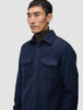 Eine Person, die ein doppellagiges Woll-Overshirt in der Farbe Regular Dark Navy über einem braunen Rollkragenpullover trägt.
