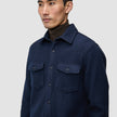 Eine Person, die ein doppellagiges Woll-Overshirt in der Farbe Regular Dark Navy über einem braunen Rollkragenpullover trägt.