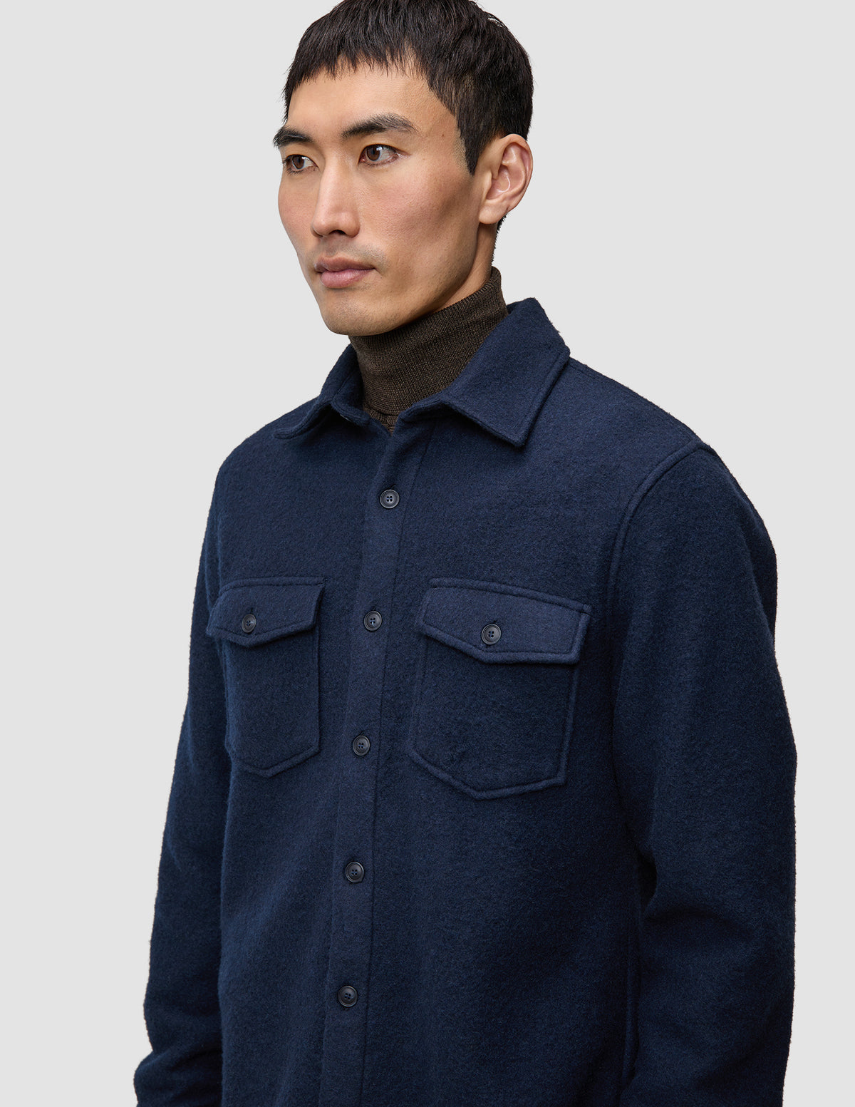 Eine Person, die ein doppellagiges Woll-Overshirt in der Farbe Regular Dark Navy über einem braunen Rollkragenpullover trägt.