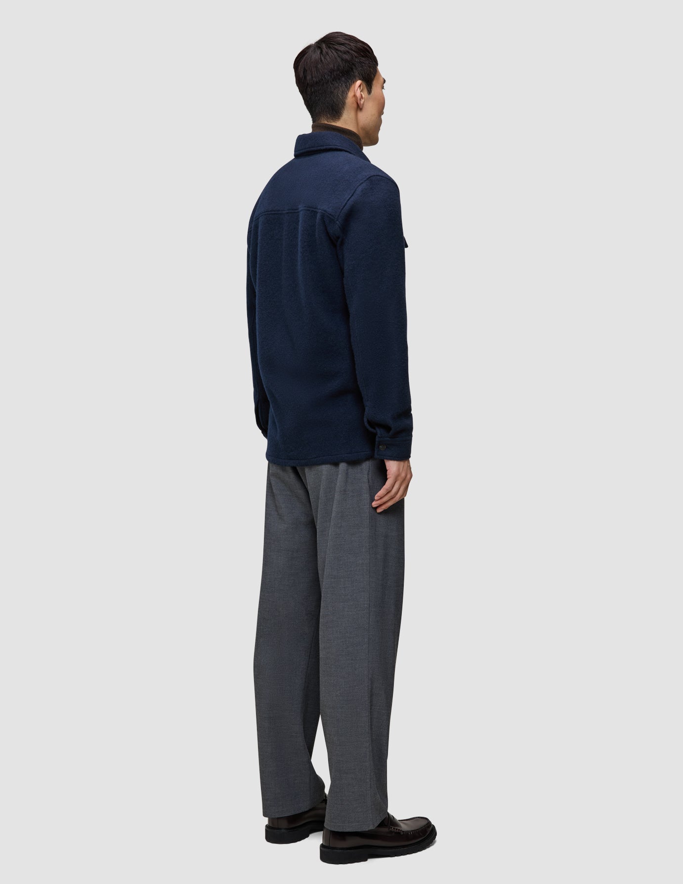 Eine Person, von hinten gesehen, die ein doppellagiges Woll-Overshirt in der Farbe Regular Dark Navy und eine graue Hose trägt.