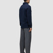 Eine Person, von hinten gesehen, die ein doppellagiges Woll-Overshirt in der Farbe Regular Dark Navy und eine graue Hose trägt.