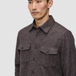 Ein Mann, der ein doppellagiges Woll-Overshirt in Sattelbraun trägt – ein braunes, doppellagiges Wollmodell mit zwei Brusttaschen, das im schlichten, skandinavischen Stil gefertigt ist.