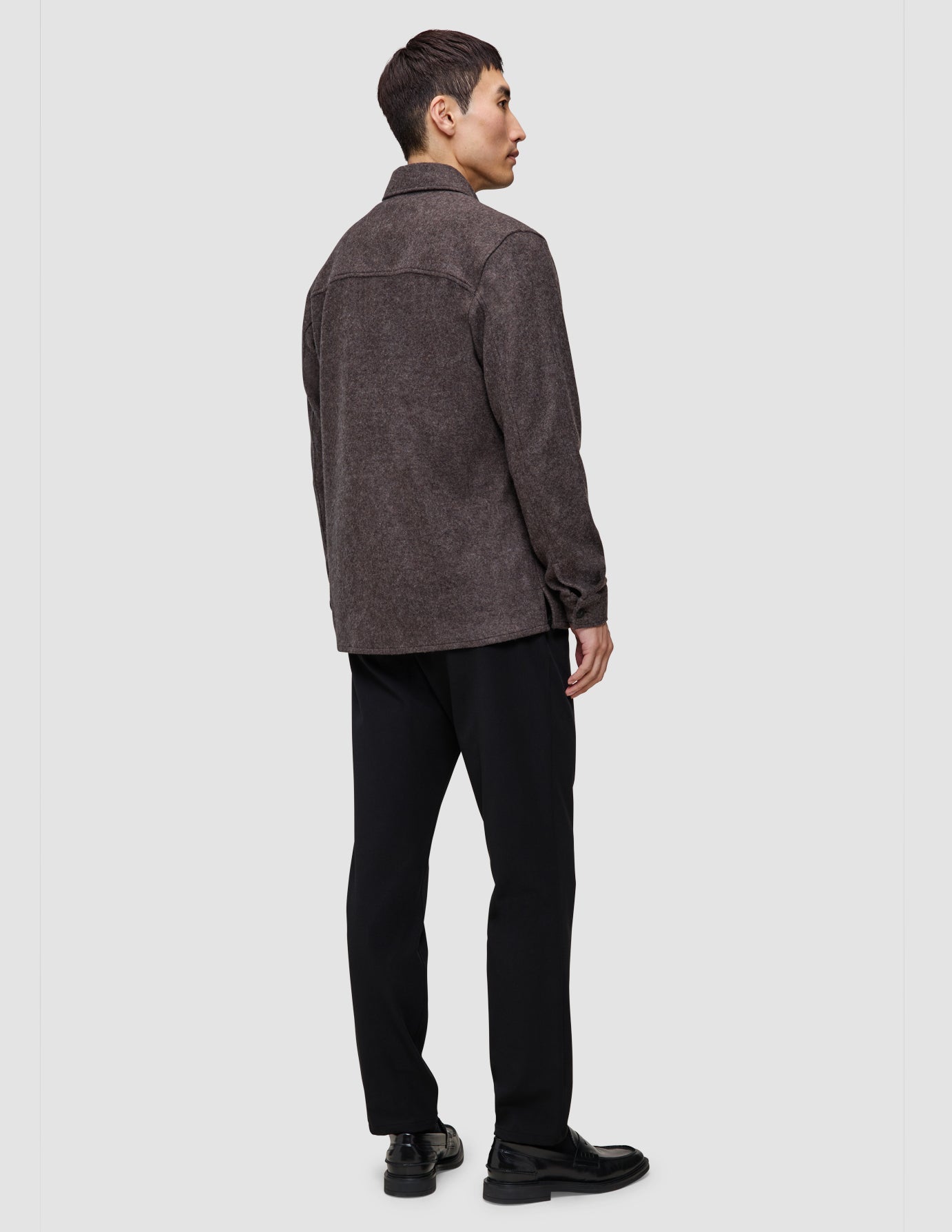 Ein Mann im Profil trägt ein doppellagiges Wollhemd in Sattelbraun über einer schwarzen Hose und schwarzen Loafern.