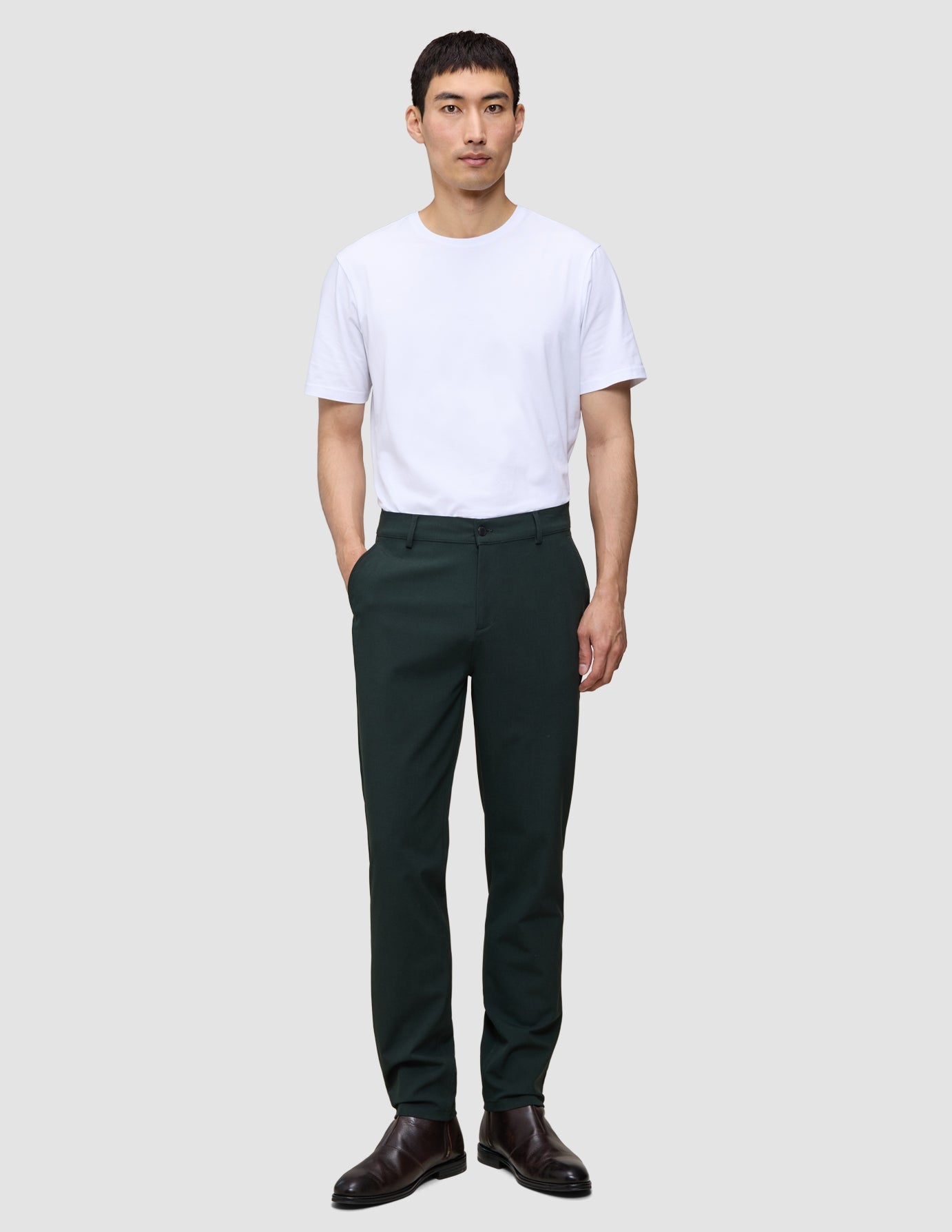 Ein Mann in einem weißen T-Shirt und einer Ease-Hose Regular Northern Pine, dazu braune Lederschuhe.