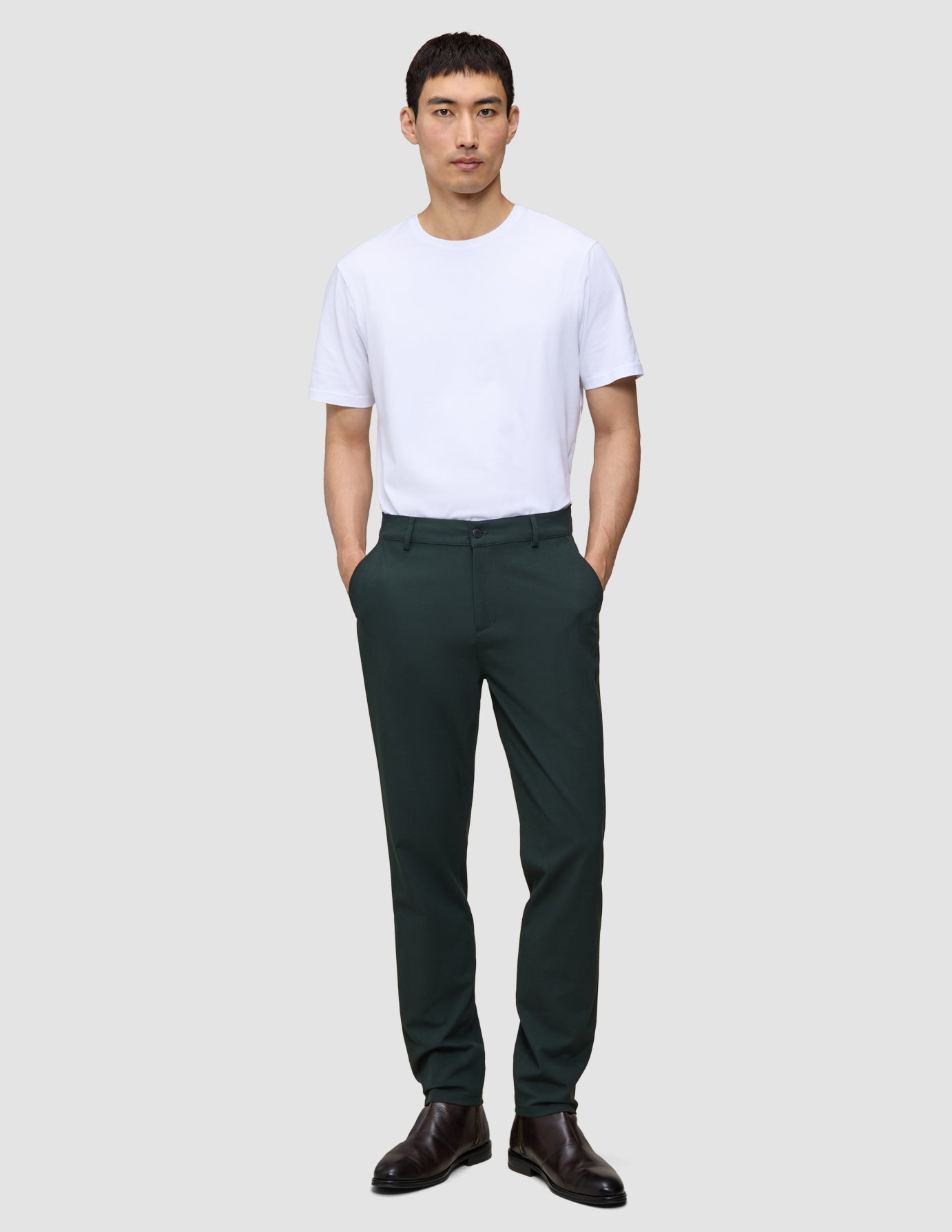Ein Mann, der ein weißes T-Shirt und eine dunkelgrüne Ease-Hose Regular Northern Pine trägt und die Hände in den Taschen hat.