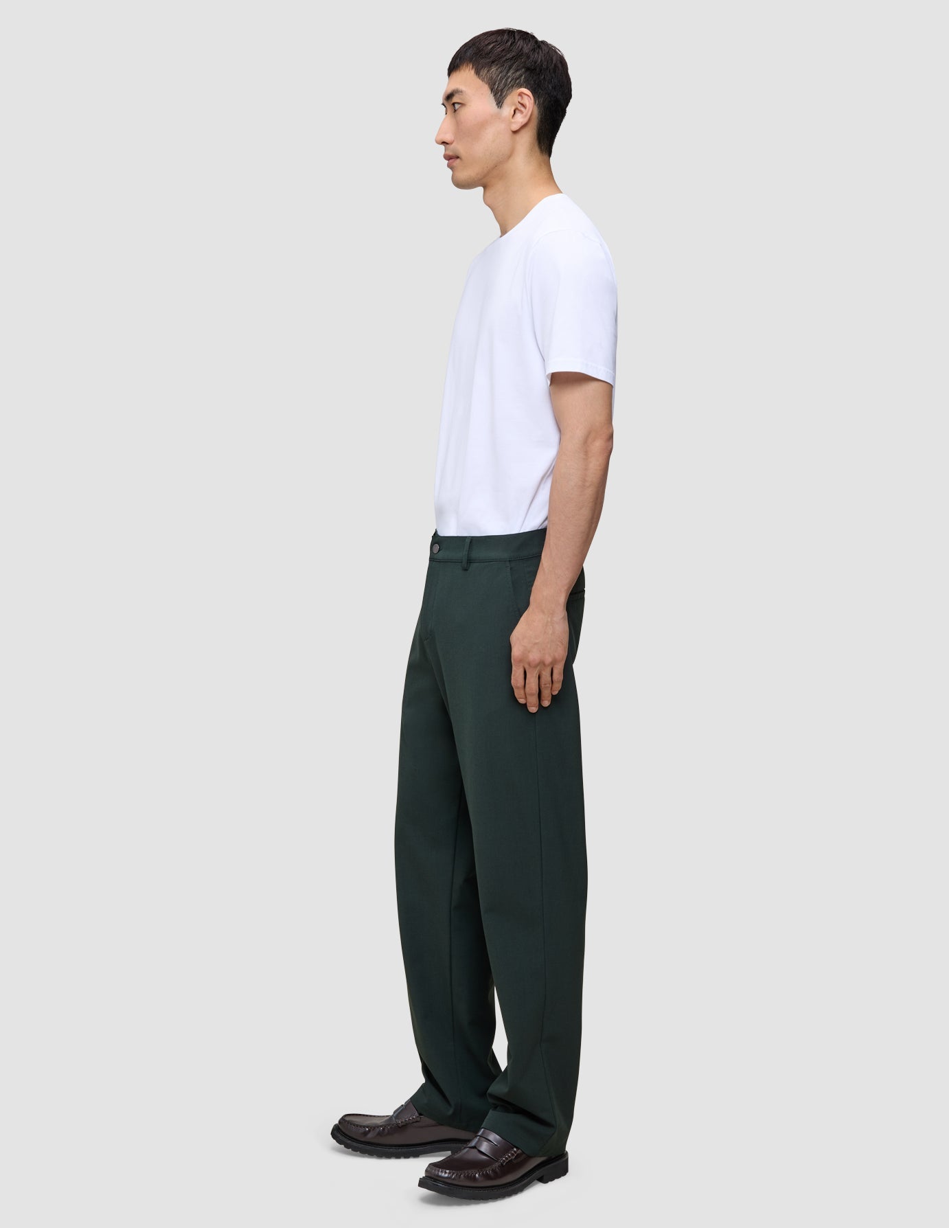 Eine Person im Profil trägt ein weißes T-Shirt, eine dunkelgrüne Ease-Hose Relaxed Fit Northern Pine und dunkelbraune Slipper.