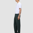 Eine Person im Profil trägt ein weißes T-Shirt, eine dunkelgrüne Ease-Hose Relaxed Fit Northern Pine und dunkelbraune Slipper.