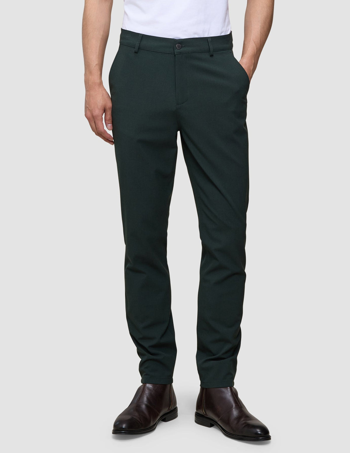 Eine Person, die eine dunkelgrüne Ease Pants Slim Northern Pine und braune Lederstiefel trägt.