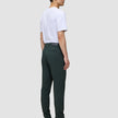 Eine Person, von hinten gesehen, die ein weißes T-Shirt und eine Ease Pants Slim Northern Pine sowie braune Lederstiefel trägt und damit das minimalistische skandinavische Design verkörpert.