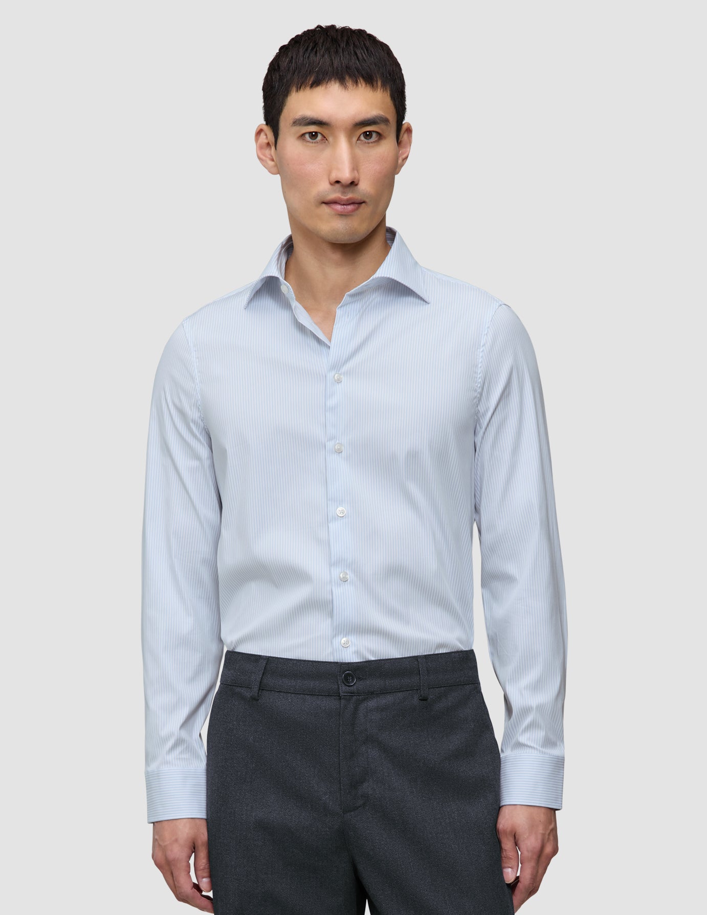 Ein Mann, der ein Elevated Shirt Regular Classic Blue Striped mit hellblauen und weißen Streifen trägt, kombiniert mit einer dunkelgrauen Hose.