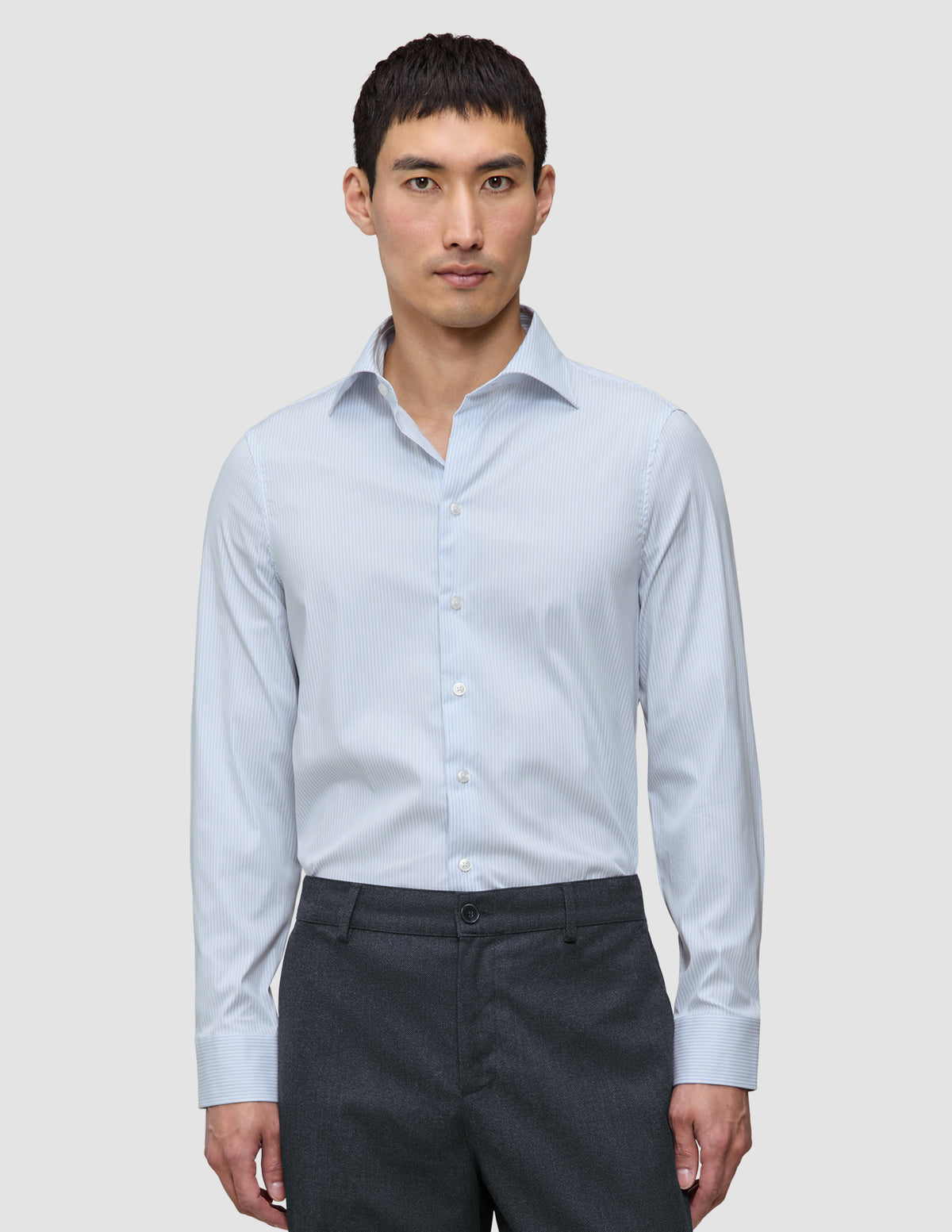 Ein Mann, der ein Elevated Shirt Regular Classic Blue Striped mit hellblauen und weißen Streifen trägt, kombiniert mit einer dunkelgrauen Hose.