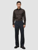 Ein Mann, der ein Elevated Shirt Regular in Dunkelbraun aus Pima-Baumwolle trägt, das in eine anthrazitfarbene Hose gesteckt ist, dazu dunkle Slipper.