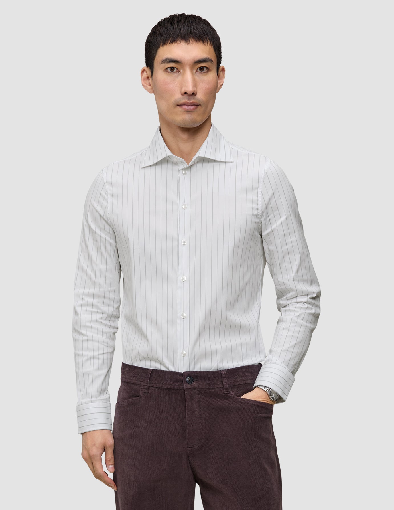 Ein Mann trägt ein hellgrau gestreiftes Elevated Shirt Regular, das er in eine dunkle Hose gesteckt hat.