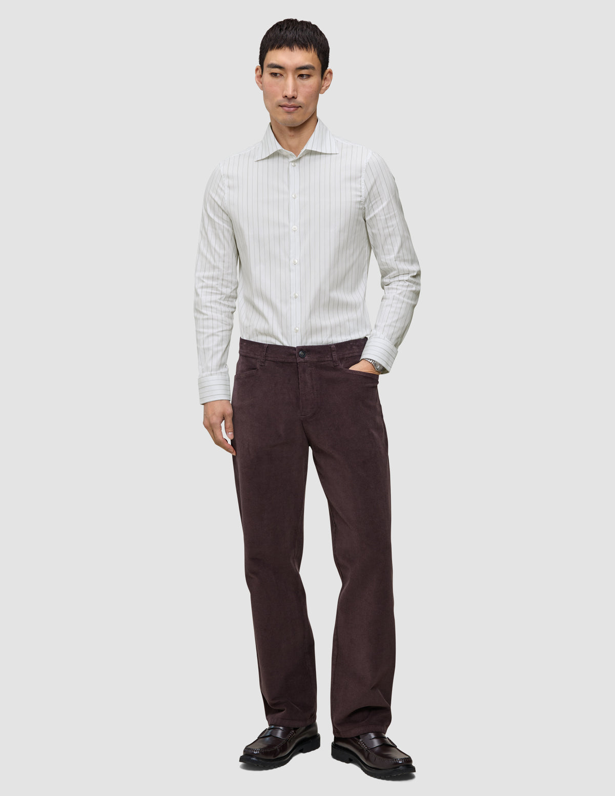 Ein Mann, der ein Elevated Shirt Regular in hellgrau gestreift aus Pima-Baumwolle trägt, dazu eine dunkle Hose und dunkle Slipper.