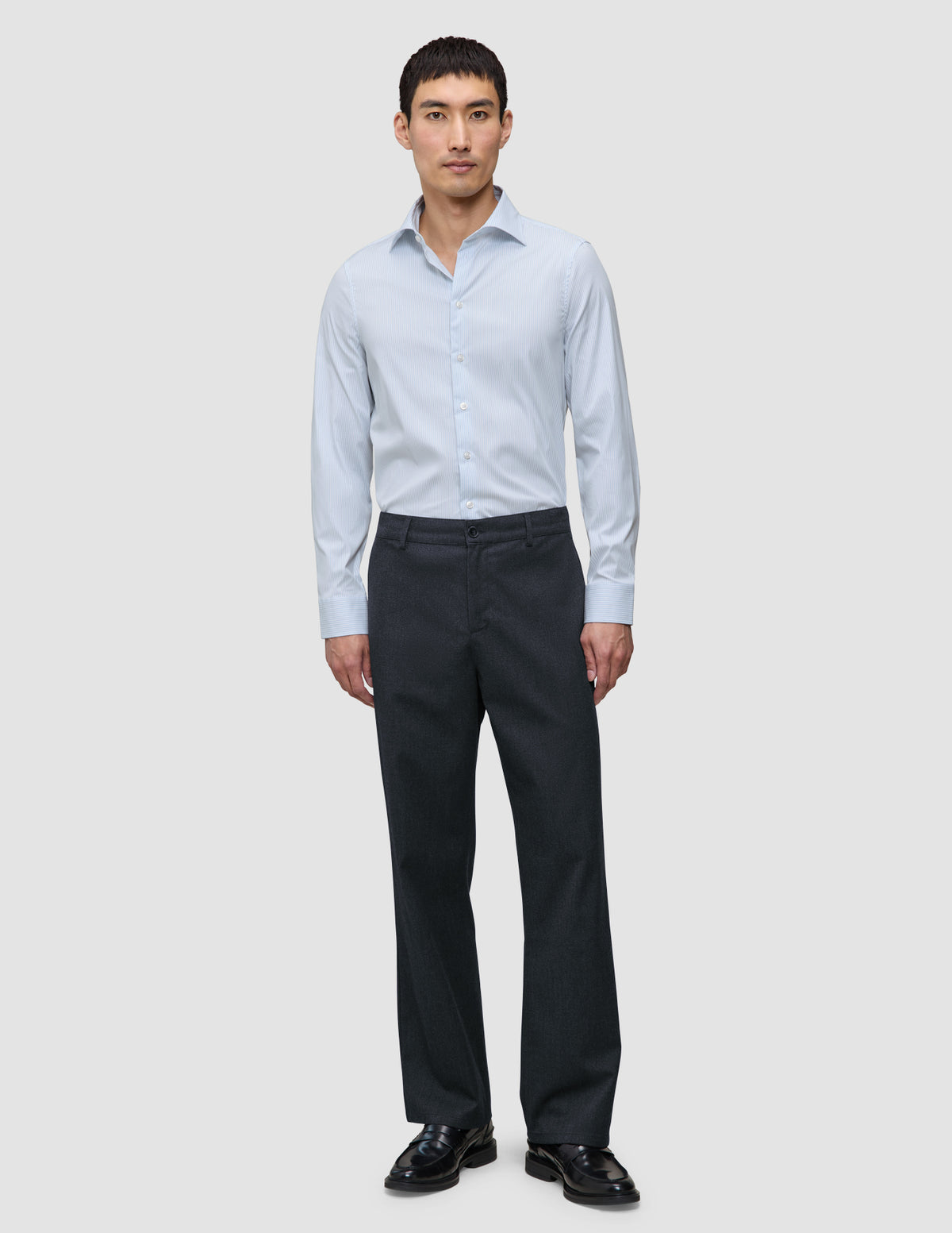Ein Mann, der ein langärmeliges Hemd der Marke Elevated im Modell Slim Classic Blue Striped, eine dunkle Hose und schwarze Slipper trägt.