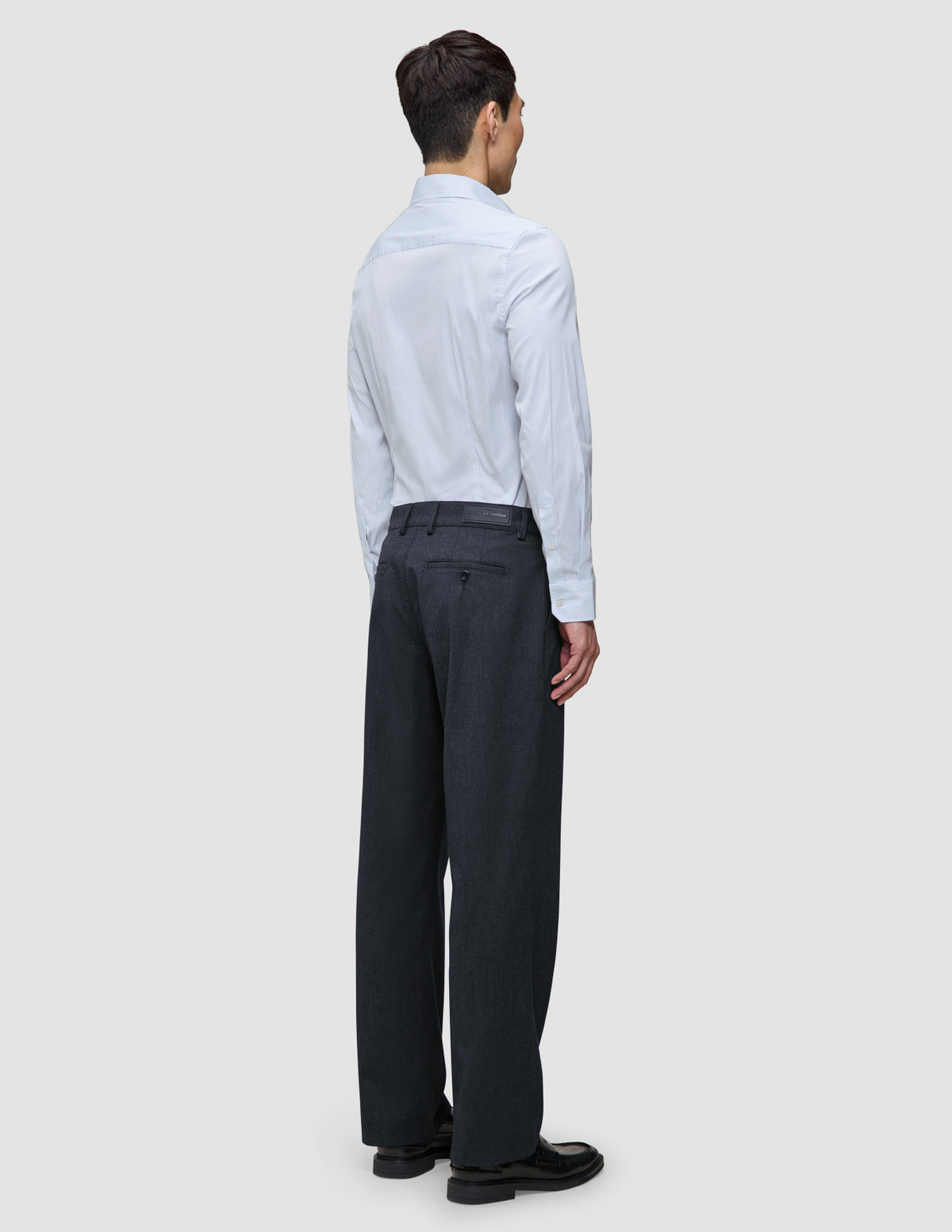 Eine Person, von hinten gesehen, die ein hellblaues, feinn gestreiftes Elevated Shirt Slim Classic Blue Striped-Hemd mit Knopfleiste trägt, das in eine dunkelgraue Hose gesteckt ist, sowie schwarze Loafer.