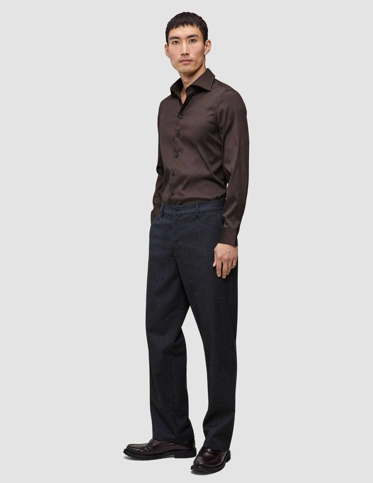 Ein Mann trägt das Elevated Shirt Slim in Dunkelbraun aus Pima-Baumwolle, dazu eine dunkle Hose und dunkle Schuhe.