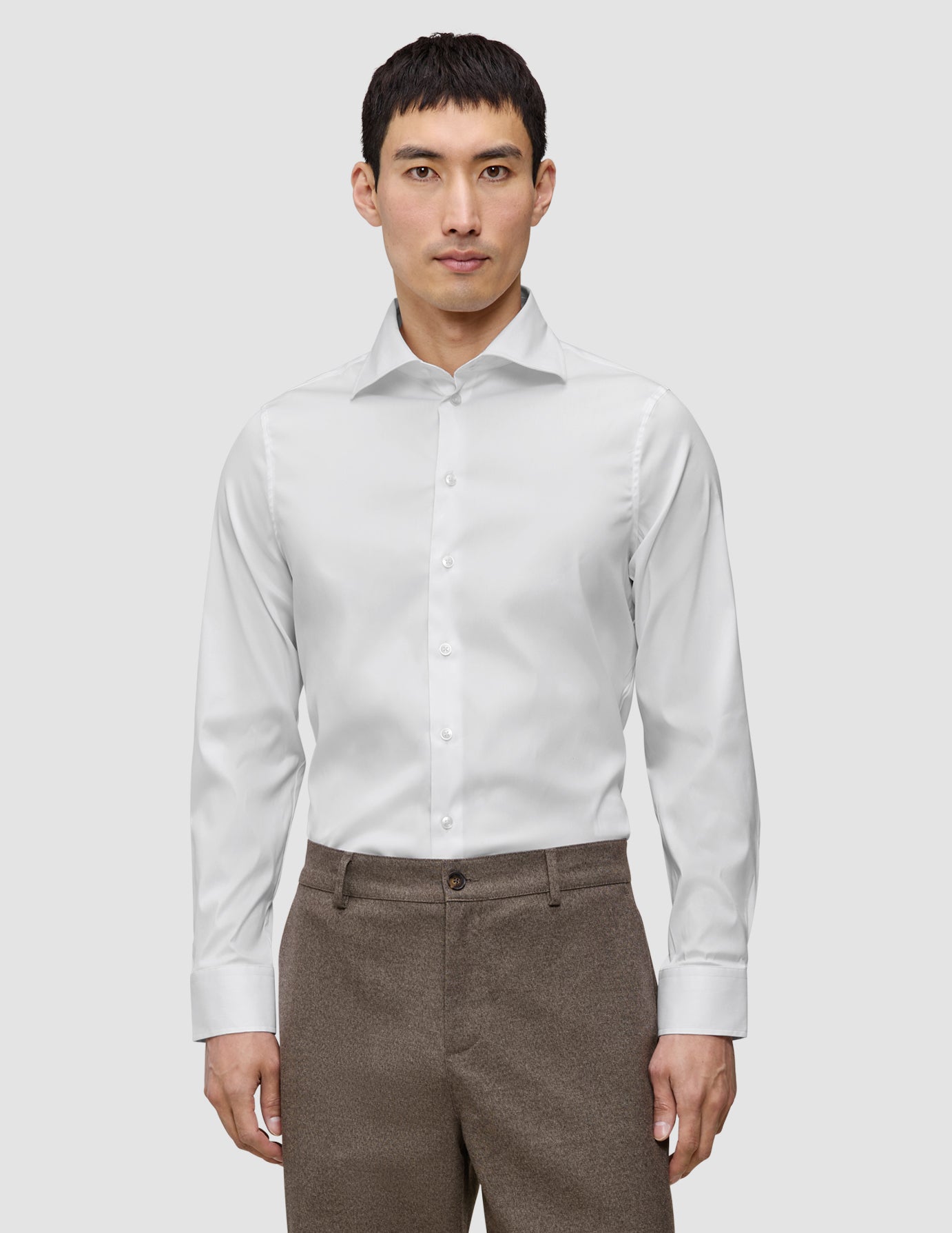 Ein Mann, der ein weißes, schmal geschnittenes Elevated-Hemd trägt, das in eine braune Hose gesteckt ist.