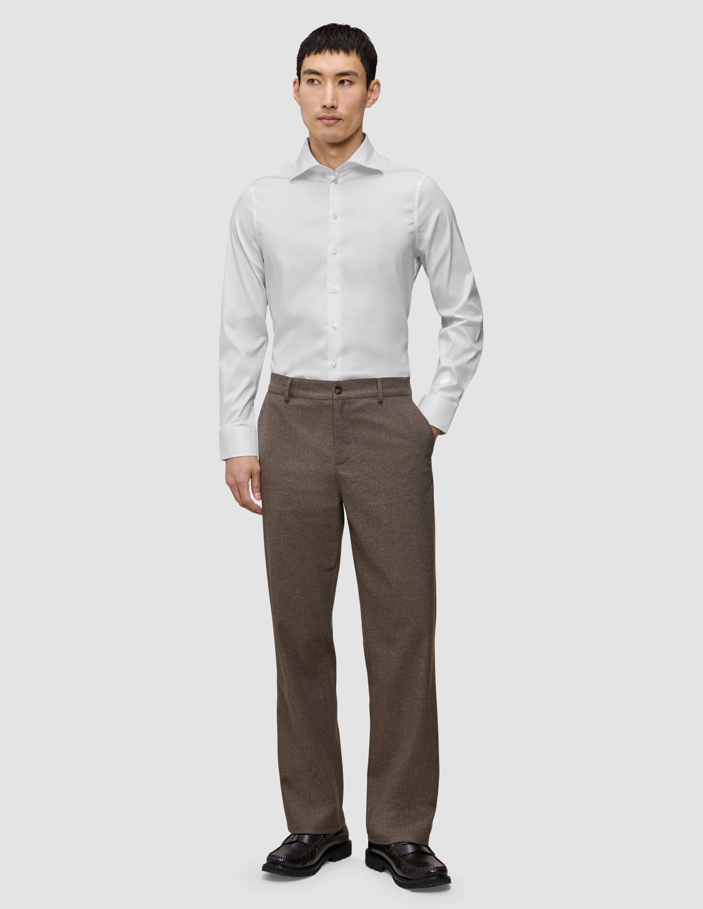 Ein Mann, der ein weißes, schmal geschnittenes Elevated-Hemd trägt, dazu eine braune Hose und dunkle Slipper.