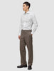Ein Mann trägt ein weißes, schmal geschnittenes Elevated Shirt mit Knöpfen, das er in eine braune Hose gesteckt hat, sowie dunkle Slipper.