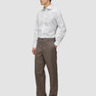 Ein Mann trägt ein weißes, schmal geschnittenes Elevated Shirt mit Knöpfen, das er in eine braune Hose gesteckt hat, sowie dunkle Slipper.