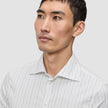 Ein Mann trägt ein Elevated Shirt Slim Light Grey Striped, ein schmal geschnittenes, hellgrau gestreiftes Button-Down-Hemd aus Pima-Baumwolle mit einem Spread-Kragen.