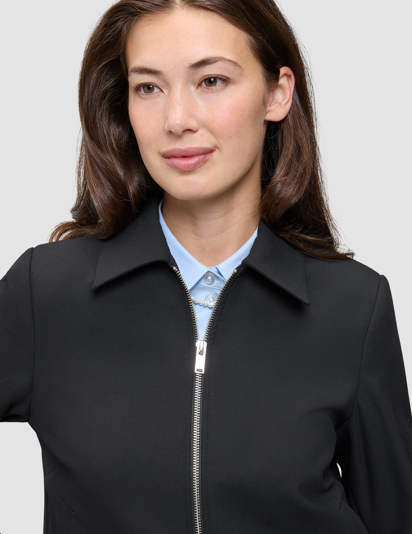 Eine Person, die eine schwarze Essential Short Zip Jacket über einem hellblauen Hemd mit Knöpfen trägt.