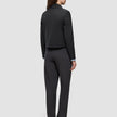 Eine Person, die von hinten zu sehen ist, trägt eine schwarze Essential Short Zip Jacket über einem hellblauen Hemd mit Kragen und einer dunkelgrauen Hose; das Design ist schlicht und minimalistisch.