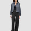 Eine Frau, die eine Essential Short Zip Jacket in Dunkelgrau-Melange über einem schwarzen Oberteil und einer schwarzen Hose mit weitem Bein trägt.