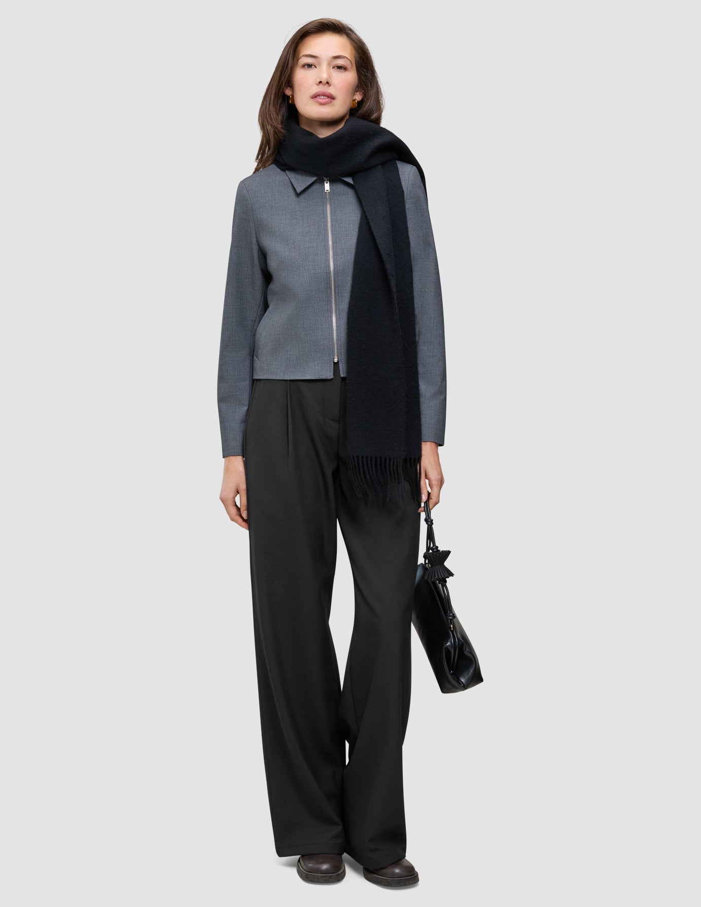 Eine Frau, die eine Essential Short Zip Jacket in Dunkelgrau-Melange, einen schwarzen Schal und eine schwarze Hose trägt und eine schwarze Handtasche bei sich hat.