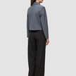 Eine Frau, von hinten gesehen, die eine Essential Short Zip Jacket in Dunkelgrau-Melange als kurze Reißverschlussjacke und eine schwarze Hose mit weitem Bein trägt.