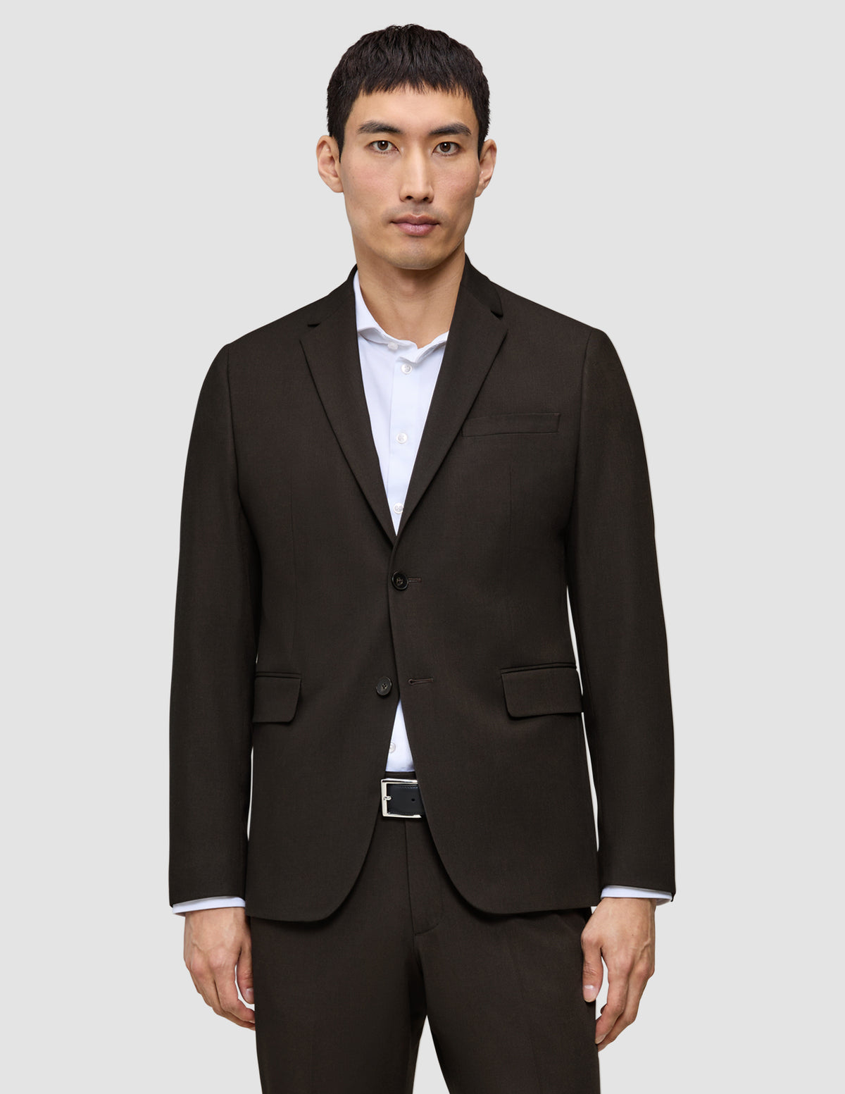 Ein Mann trägt einen dunkelbraunen Motion Blazer Regular Cognac mit 360°-Stretch über einem weißen Hemd mit Knöpfen, was ein klares, skandinavisches Design widerspiegelt.