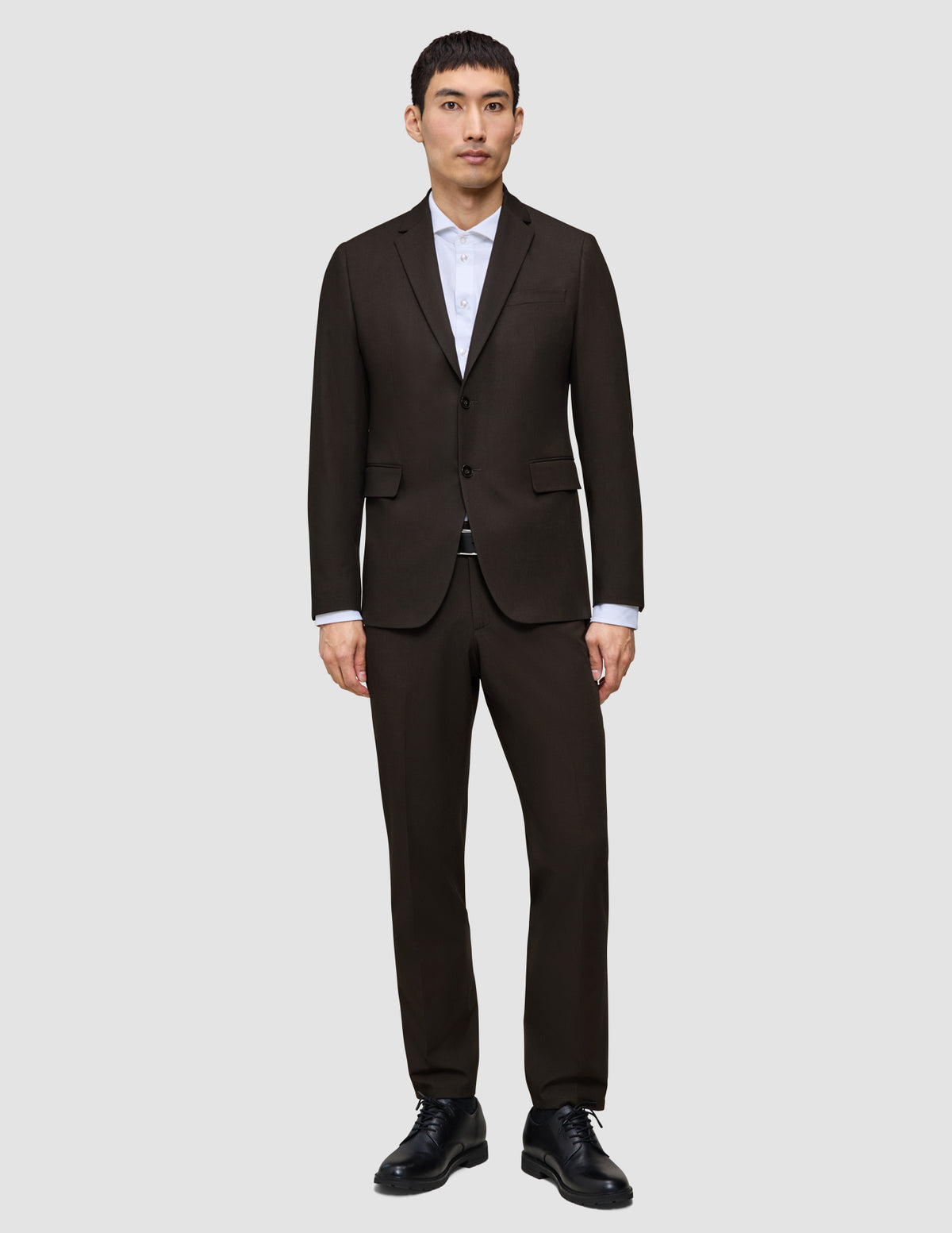 Ein Mann trägt einen dunkelbraunen Motion Blazer Regular Cognac über einem weißen Hemd mit Kragen und dazu schwarze Anzugschuhe, was eine klare, skandinavische Designästhetik widerspiegelt.