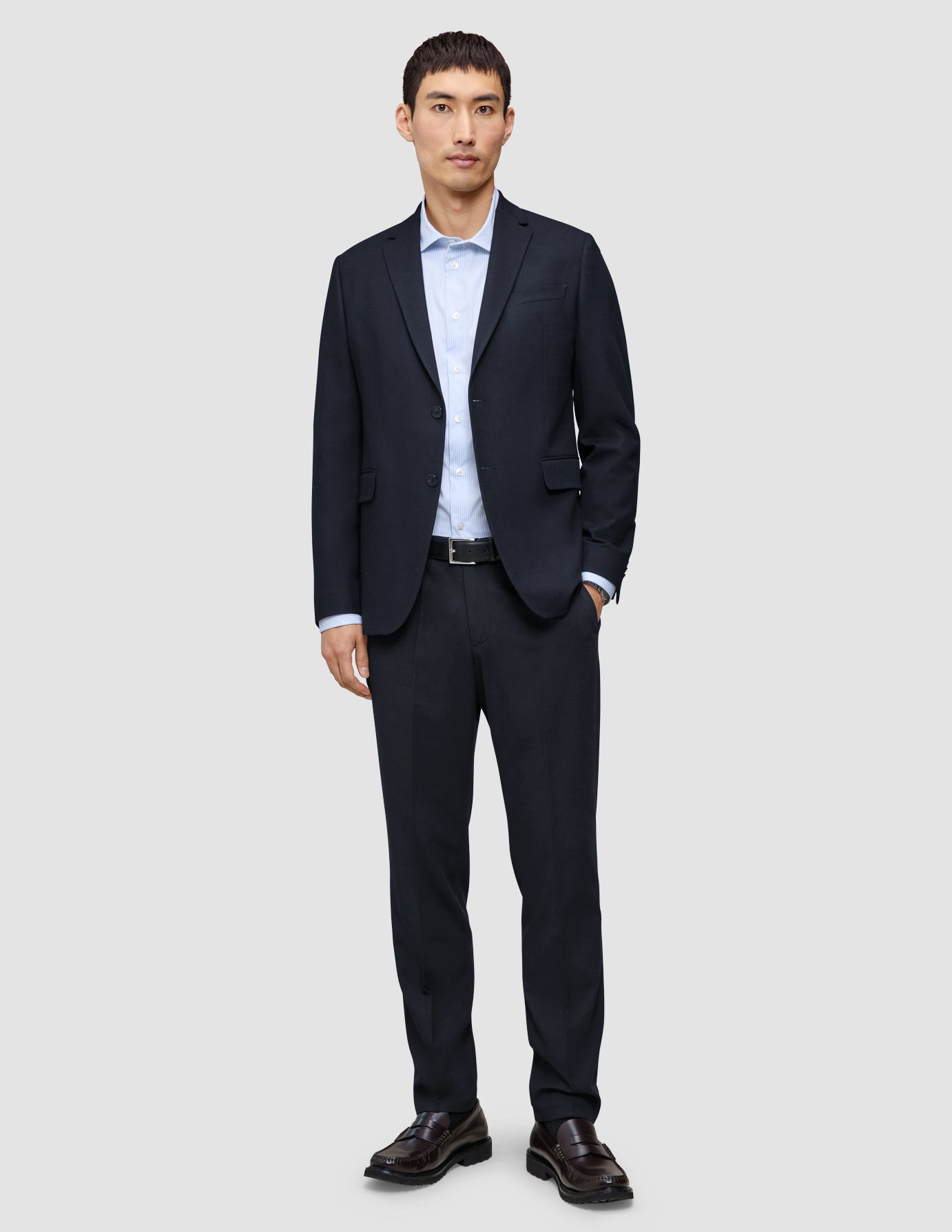 Ein Mann, der einen Motion Blazer Regular in Mitternachtsblau, eine dazu passende Hose, ein hellblaues Hemd mit Knöpfen und dunkle Slipper trägt.