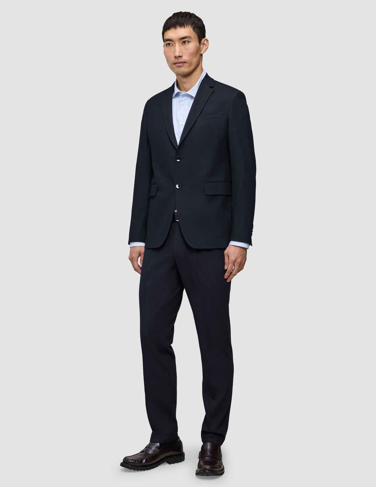 Ein Mann trägt einen Motion Blazer Regular in Mitternachtsblau mit 360°-Stretch und eine dazu passende Hose über einem hellblauen Hemd, dazu dunkle Loafer.