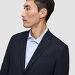 Eine Person im Profil, von der Brust aufwärts, die einen Motion Blazer Regular in Mitternachtsblau über einem hellblau gestreiften Hemd trägt.