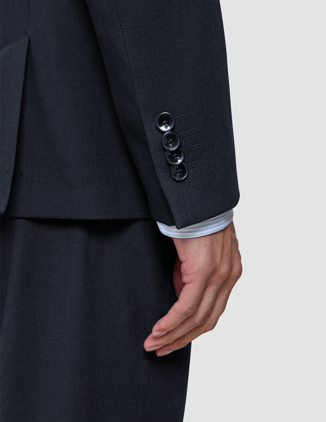 Nahaufnahme eines Ärmels des Motion Blazer Regular in Mitternachtsblau mit vier Manschettenknöpfen, unter dem der Ärmel eines weiß gestreiften Hemdes hervorblitzt – ein Beispiel für skandinavisches Design.