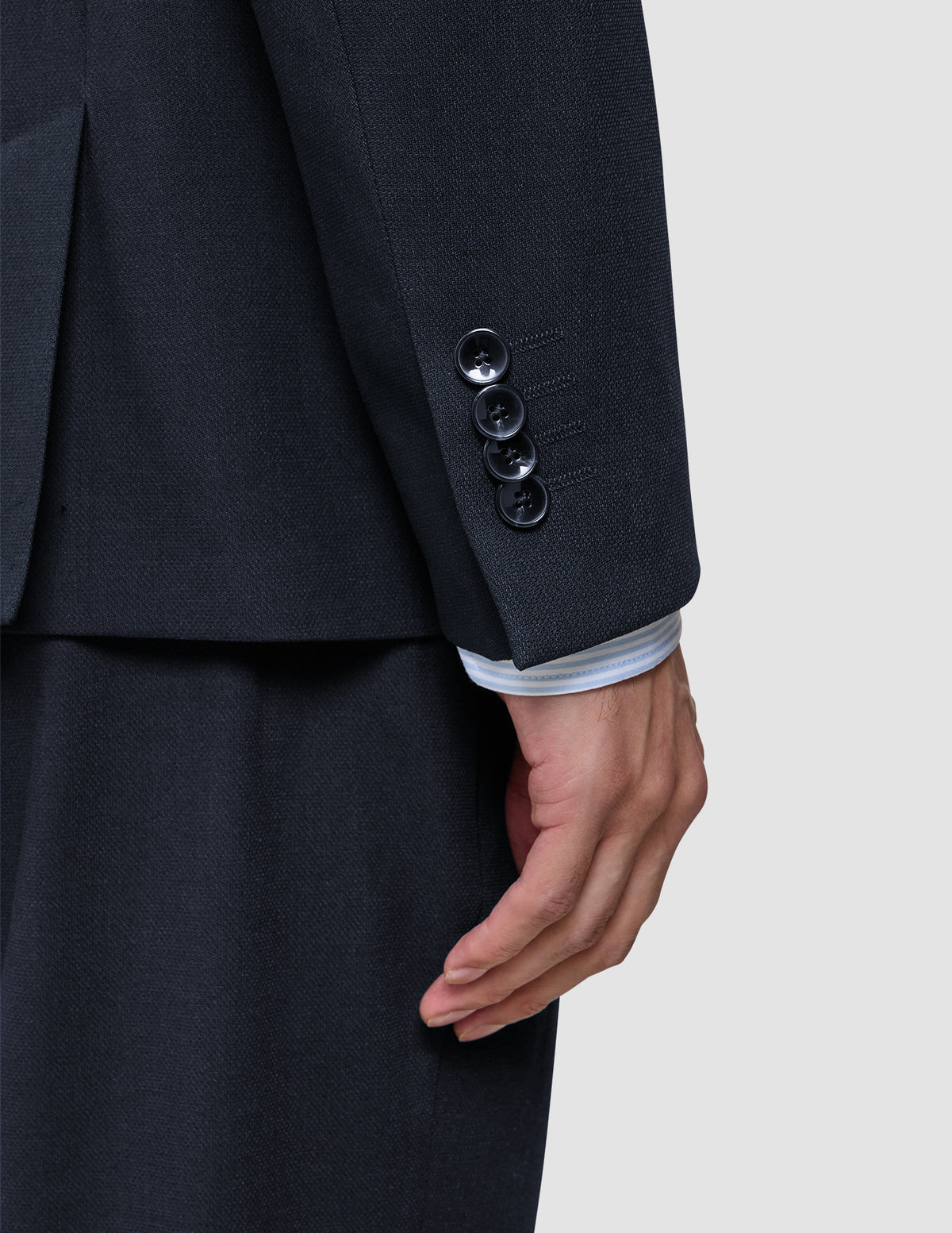 Nahaufnahme eines Ärmels des Motion Blazer Regular in Mitternachtsblau mit vier Manschettenknöpfen, unter dem der Ärmel eines weiß gestreiften Hemdes hervorblitzt – ein Beispiel für skandinavisches Design.