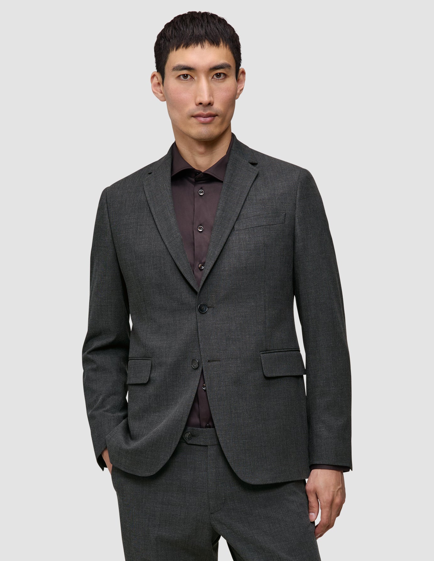 Ein Mann, der einen Motion Blazer Regular Pepper Grey über einem dunklen Hemd mit Knopfleiste trägt, das sich durch eine schlichte, skandinavische Ästhetik und ein 360°-Stretchmaterial auszeichnet.