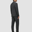 Eine Person im Profil trägt einen anthrazitfarbenen Motion Blazer Regular Pepper Grey mit 360°-Stretch und dunkle Slipper, die ein elegantes, skandinavisches Design präsentieren.