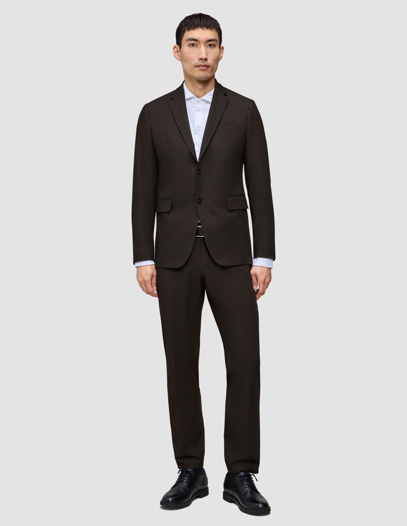 Ein Mann, der einen Motion Blazer Slim Cognac über einem weißen Hemd mit Kragen und schwarzen Anzugschuhen trägt und damit eine klare, skandinavische Designästhetik verkörpert.