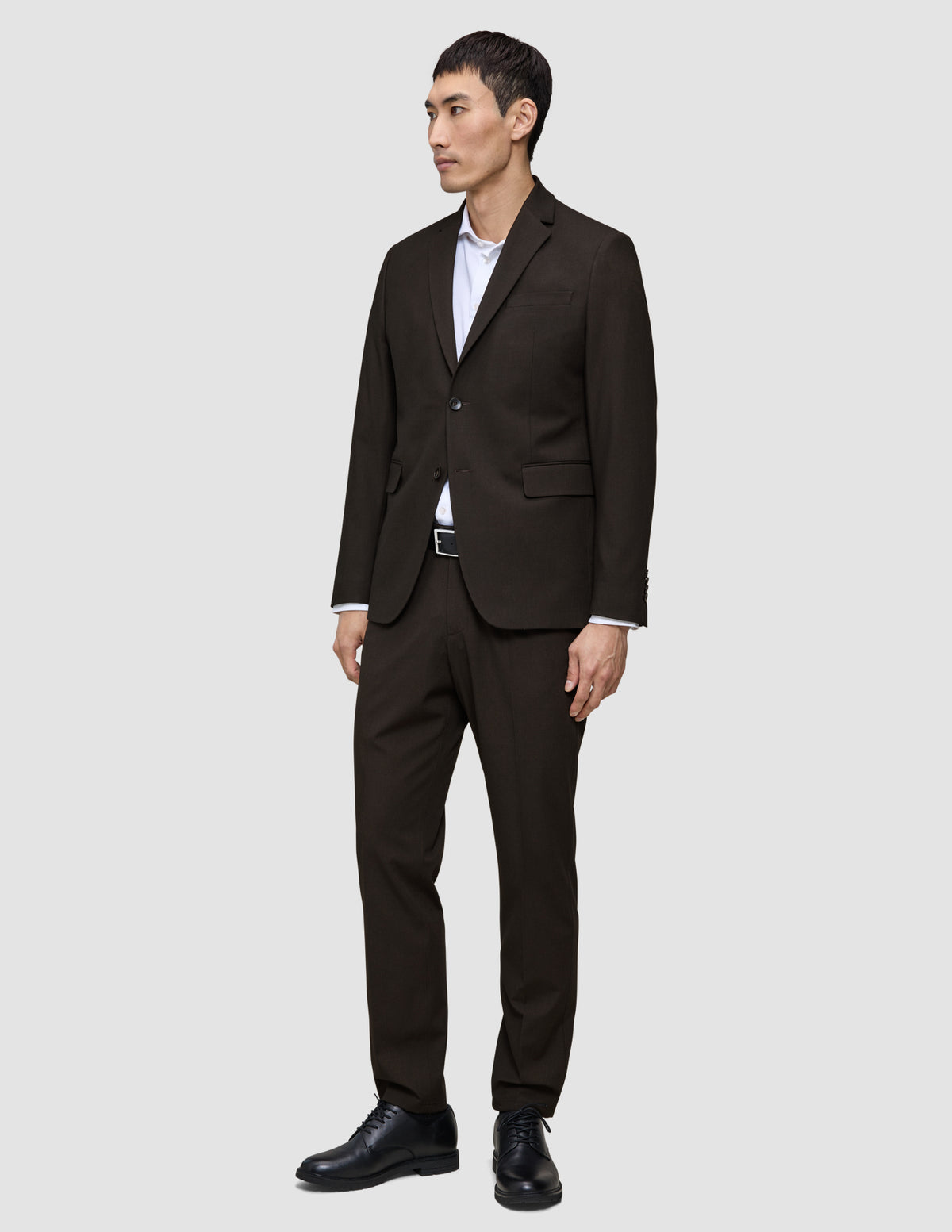 Ein Mann, der einen dunkelbraunen Motion Blazer Slim Cognac, ein weißes Hemd und schwarze Anzugschuhe trägt.