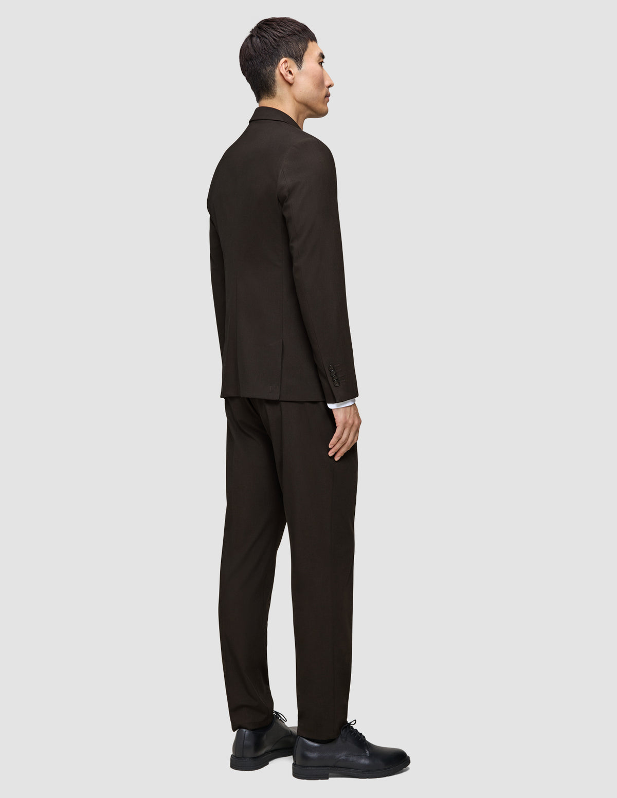 Ein Mann, der einen dunkelbraunen Motion Blazer Slim Cognac und ein weißes Hemd trägt, von der Seite gesehen, mit dunklen Anzugschuhen.