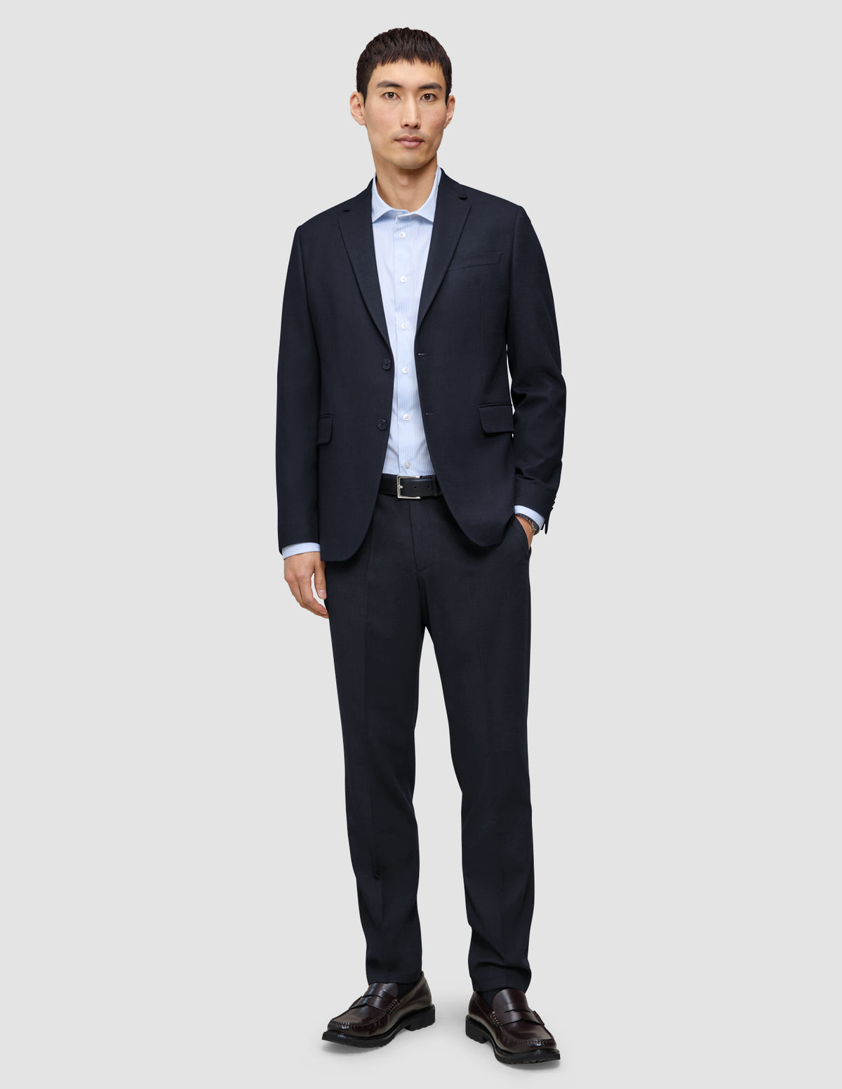 Ein Mann, der einen Motion Blazer Slim in Mitternachtsblau trägt, dazu ein hellblaues Button-Down-Hemd, eine dunkelblaue Hose, einen schwarzen Gürtel und dunkle Slipper.