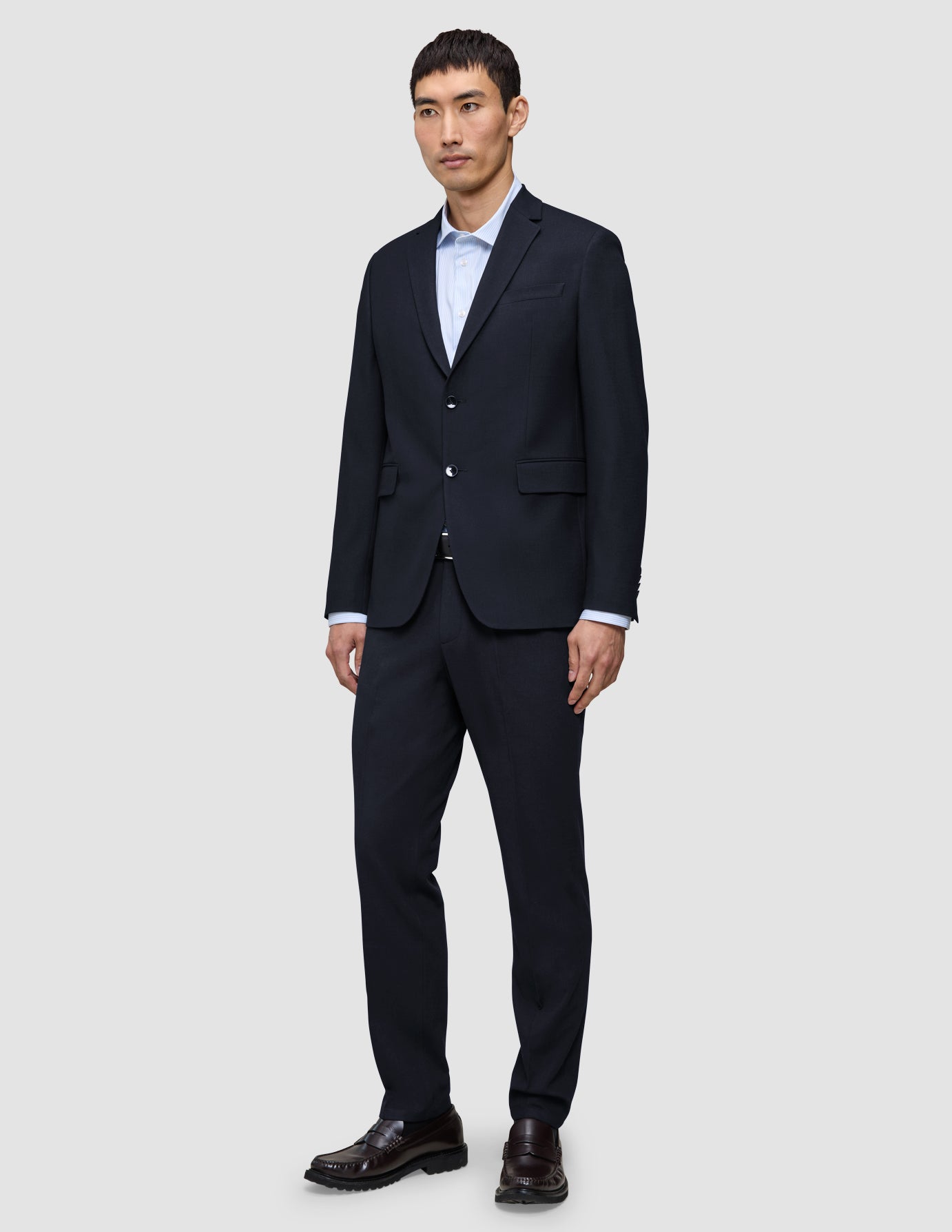 Ein Mann, der einen Motion Blazer Slim in Mitternachtsblau aus 360°-Stretch-Material, ein hellblaues Hemd mit Knöpfen und dunkle Slipper trägt.