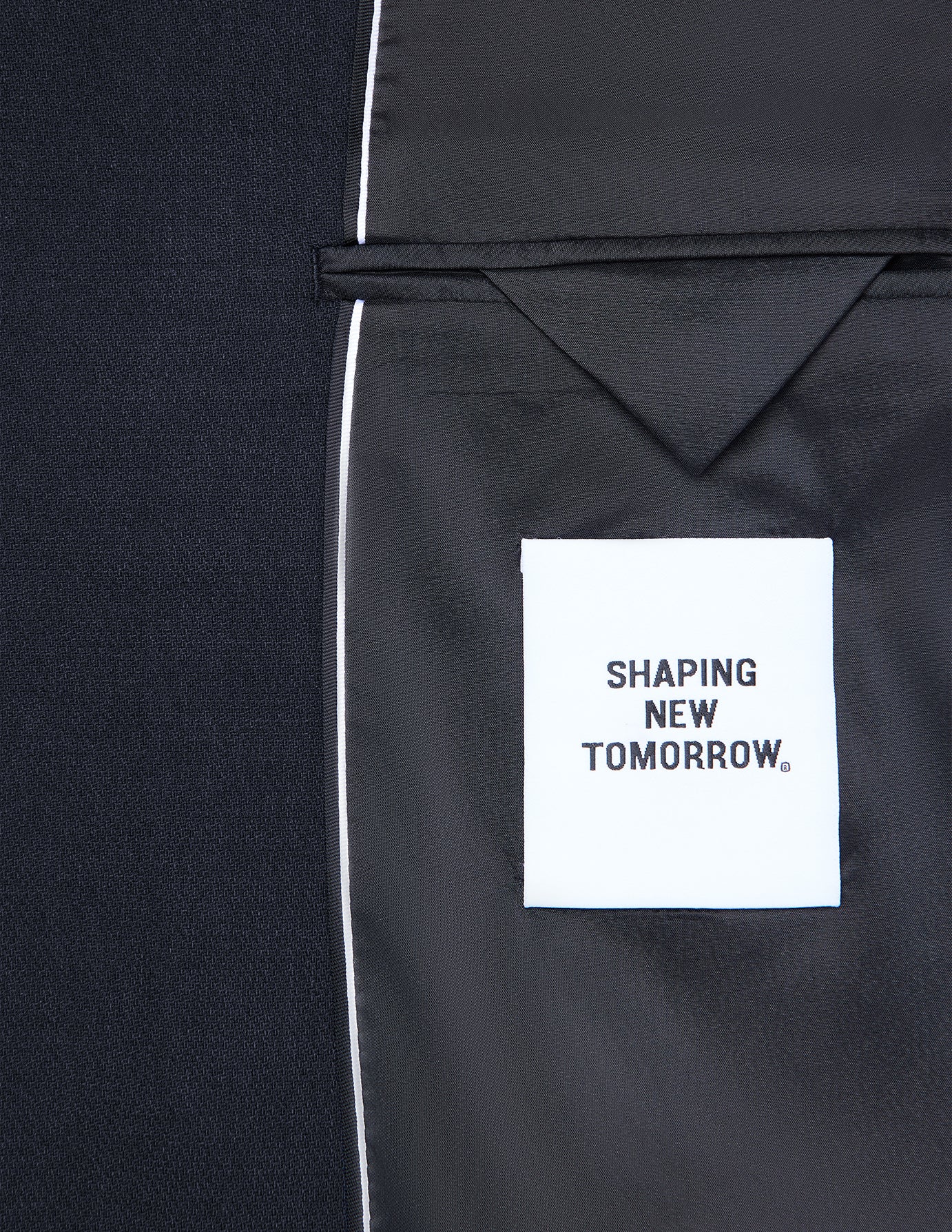 Innenseite eines dunkelblauen Motion Blazer Slim Midnight Blue mit einem weißen Stoffetikett mit der Aufschrift SHAPING NEW TOMORROW, das klassisches skandinavisches Design widerspiegelt.