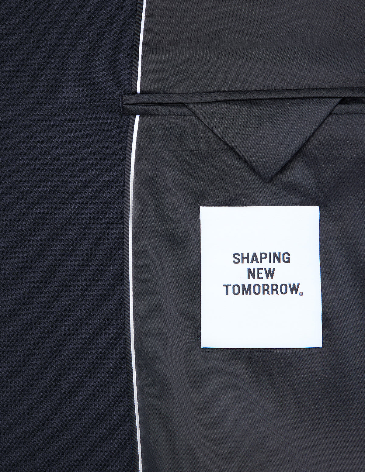 Innenseite eines dunkelblauen Motion Blazer Slim Midnight Blue mit einem weißen Stoffetikett mit der Aufschrift SHAPING NEW TOMORROW, das klassisches skandinavisches Design widerspiegelt.