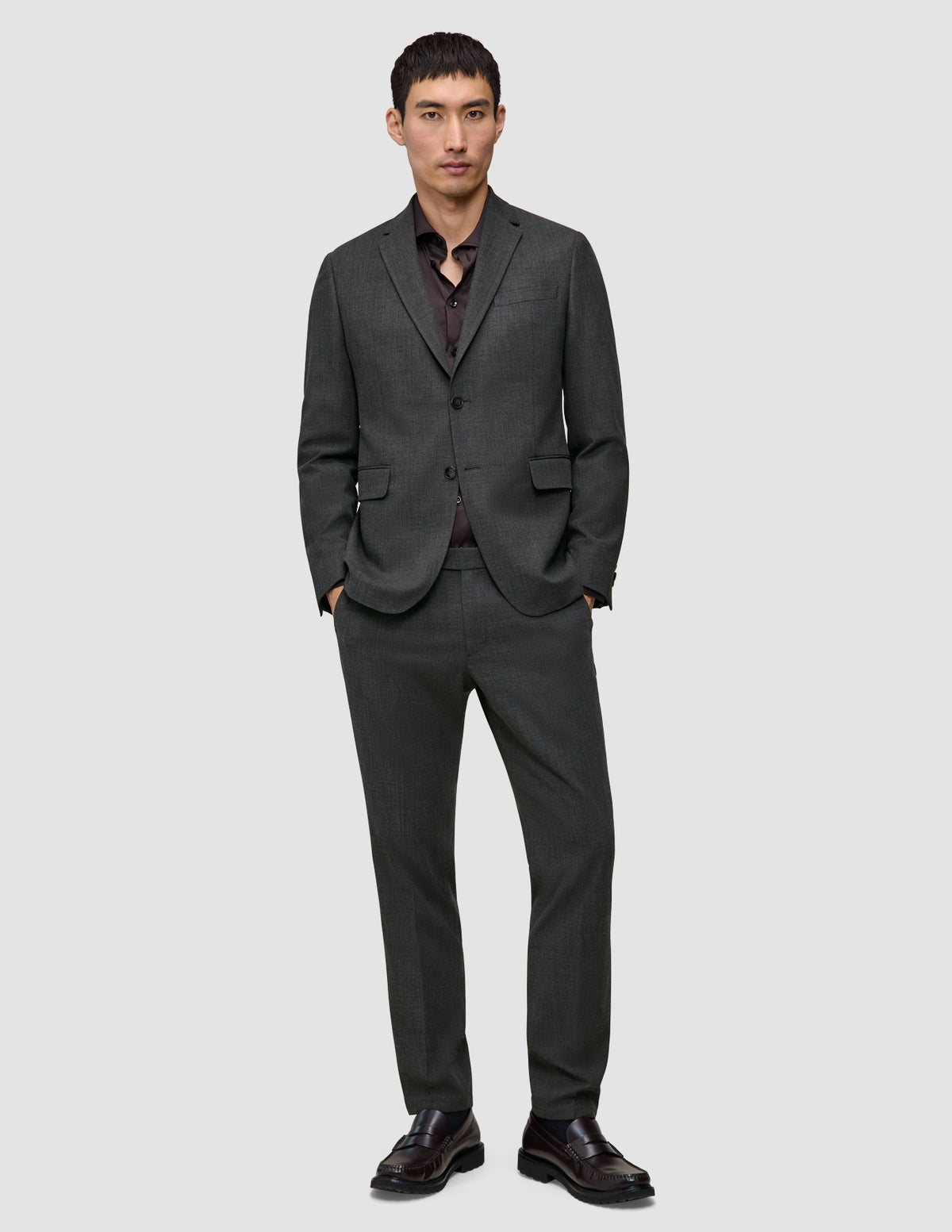 Ein Mann, der einen Motion Blazer Slim in der Farbe Pepper Grey mit einer dazu passenden Hose, einem dunklen Hemd mit Knöpfen und dunkelbraunen Loafern trägt.