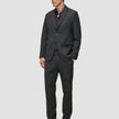 Ein Mann, der einen Motion Blazer Slim Pepper Grey mit einer Hose mit 360°-Stretch, ein dunkles Hemd mit Knopfleiste und Leder-Loafer trägt, die das minimalistische skandinavische Design widerspiegeln.