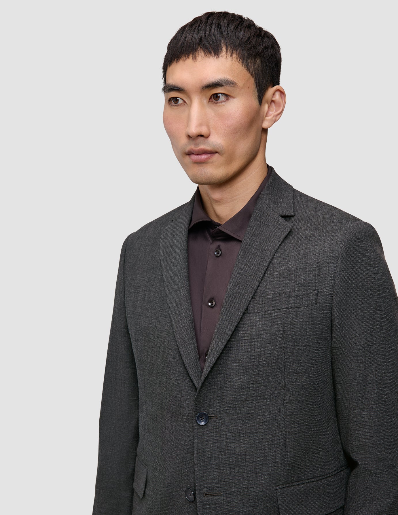 Ein Mann, der einen Motion Blazer Slim in der Farbe Pepper Grey aus 360°-Stretchstoff über einem dunklen Hemd mit Knopfleiste trägt – ein Design, das sich durch eine klare, skandinavische Ästhetik auszeichnet.